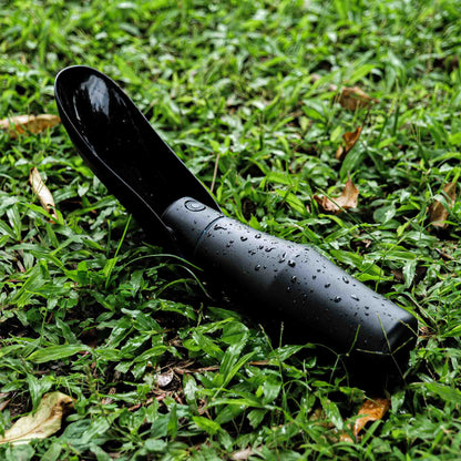 Black portable dog water bottle with a bowl on grass, ideal for outdoor pet hydration.