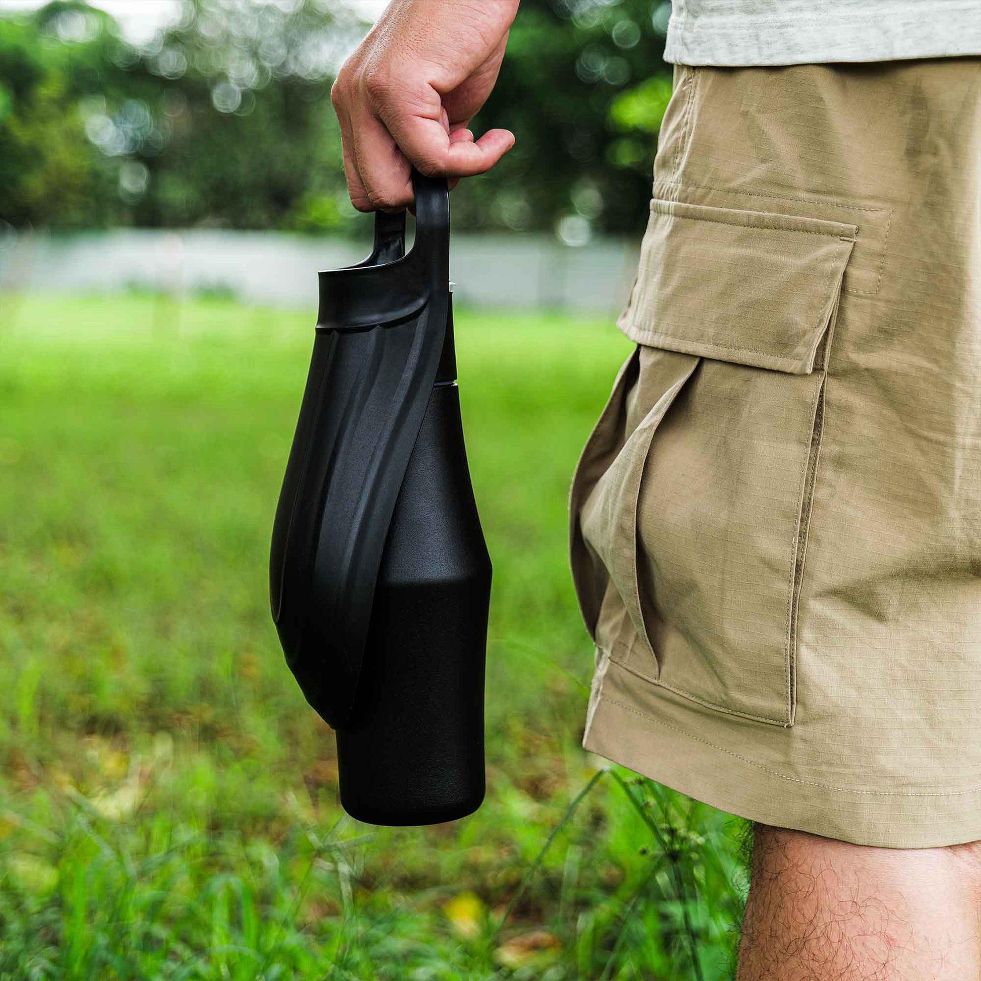 Person holding a black portable dog water bottle in a grassy area for outdoor pet use.